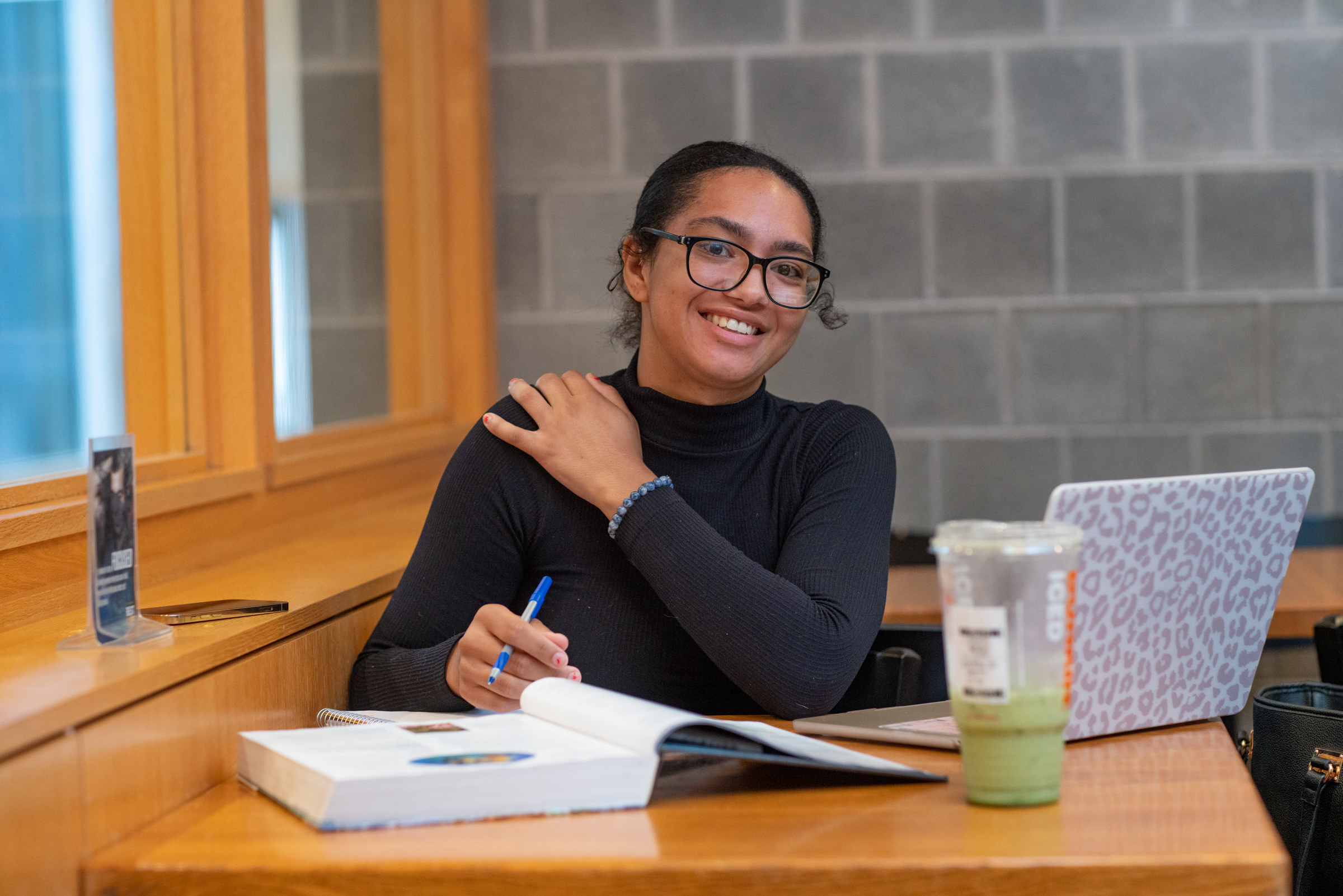 Woman looking directly at the camer and smiling. She is at a table studying. 